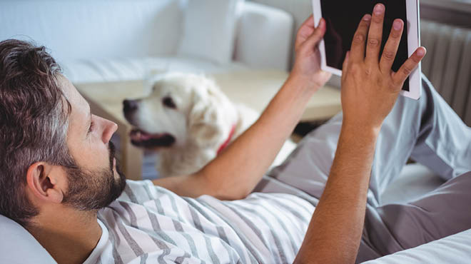 说谎在有片剂的沙发的人,和他的狗在附近